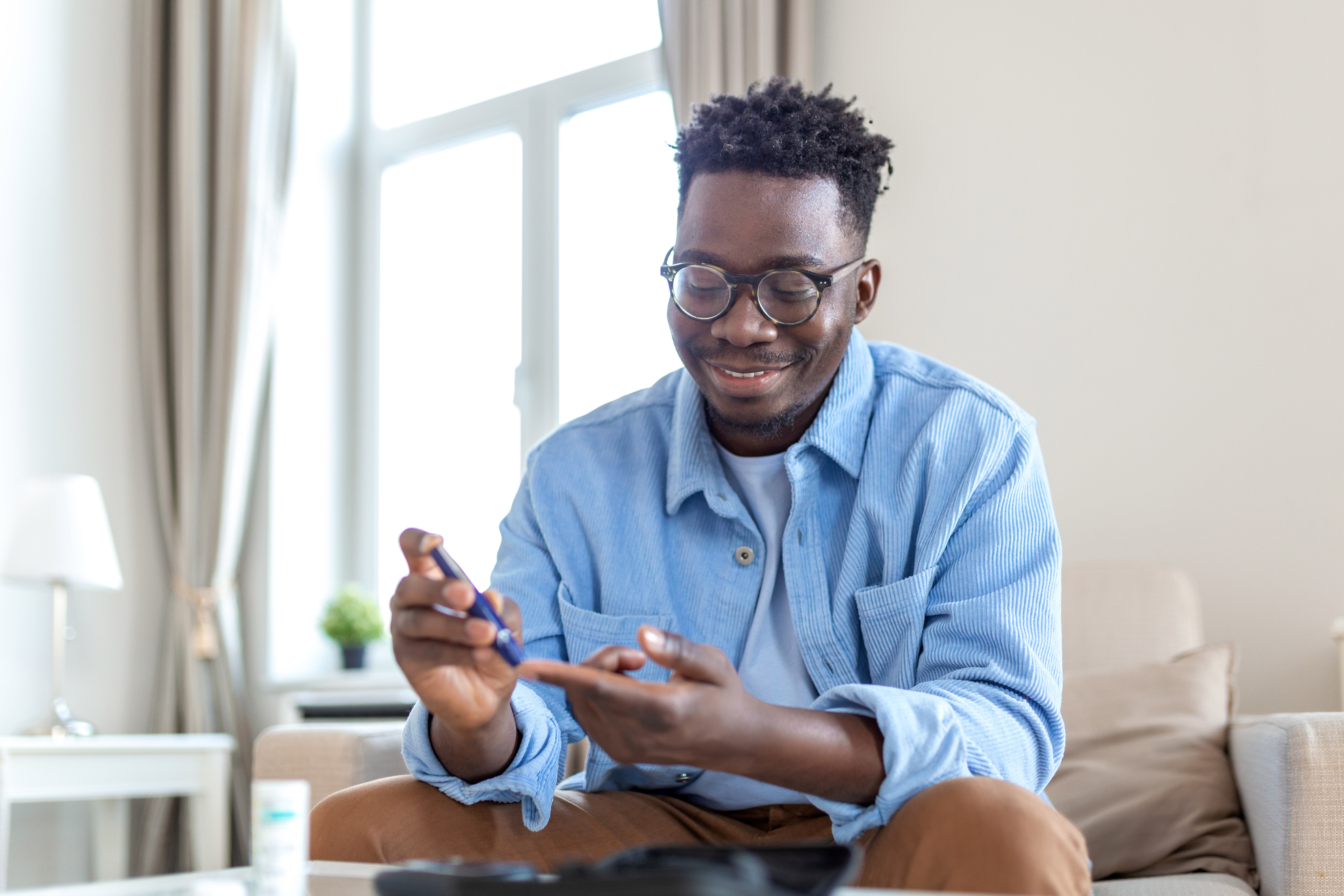 A young man checks his blood sugar while sitting on the couch.